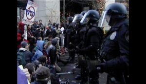 A group of police officers in riot gear confront protesters.
