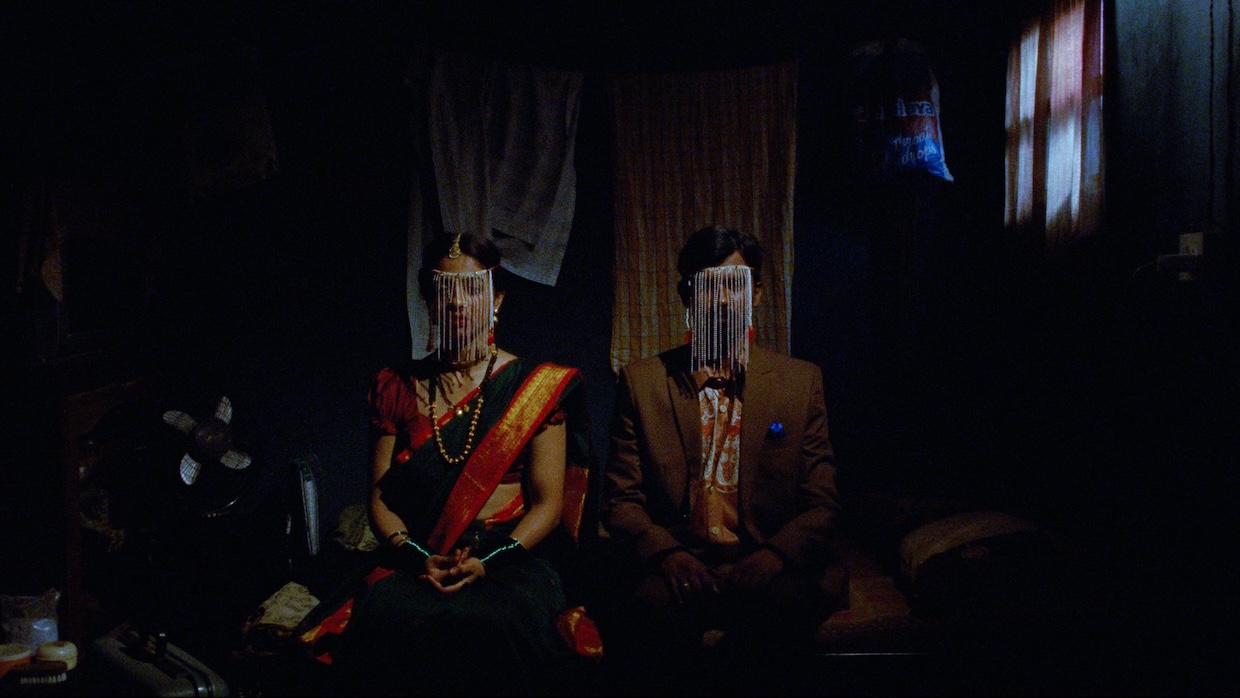 An Indian couple sit in a dark room.