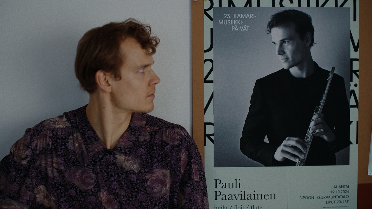 A flautist stares at a poster of himself.