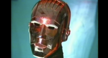A robot's shiny brass head seen in a video frame.