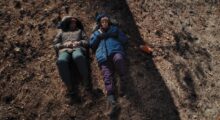 Two women are seen from above while lying in a field.