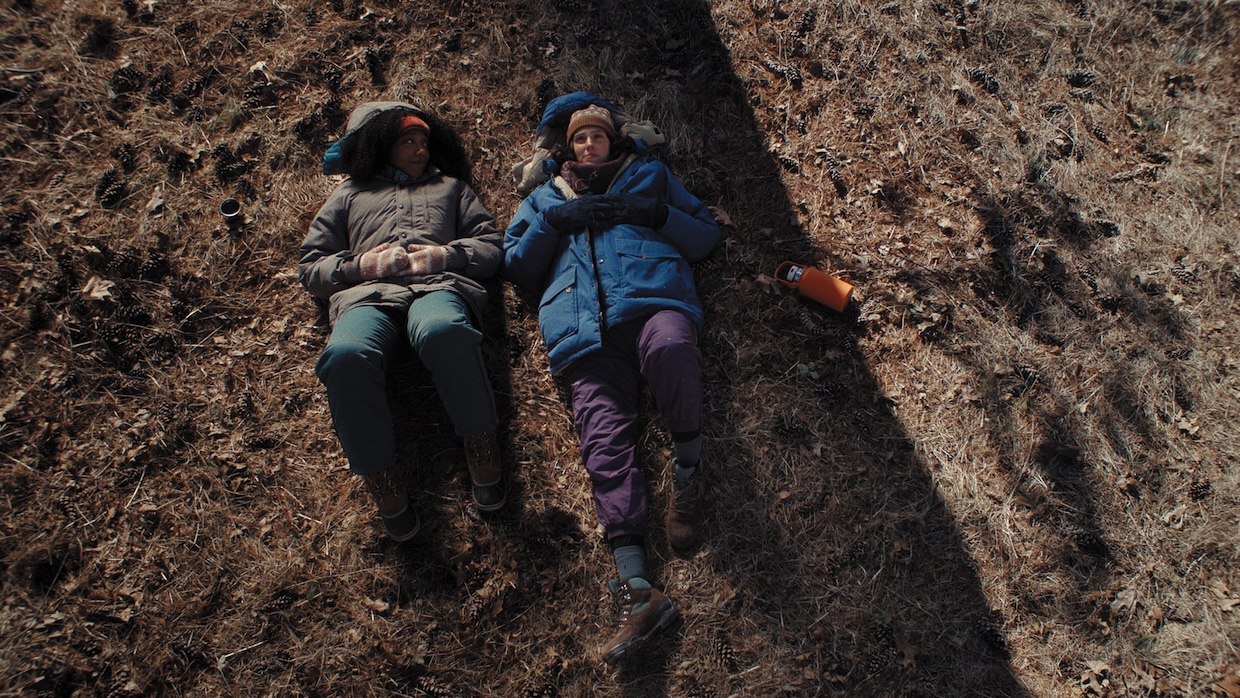 Two women are seen from above while lying in a field.
