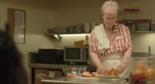 An older woman prepares a dessert in a kitchen.