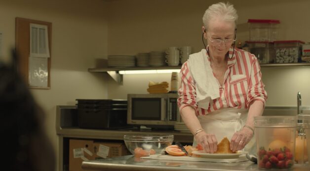 An older woman prepares a dessert in a kitchen.