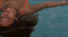 A teenage girl with dirty blond hair floats in a swimming pool in a close-up shot.