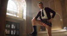 A man with heart-covered underwear stands with one foot planted on a column.