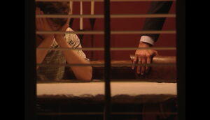A man holds his head in his hands while a man rests his hands on a chair next to him.