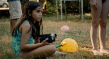 A young girl in a swimsuit holds a videocamera.