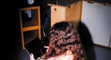 A woman sits in a chair reading a tablet.