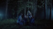 A group of goth young women sit in a circle in the forest.
