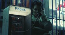 Teyana Taylor has short black hair and wears a khaki jacket. She holds a payphone to her ear and looks off in the distance.