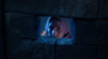 A young woman looks through a small hole in a stone wall.