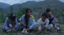 A group of adolescent Chinese girls sit on a hill during a foggy dusk. A mountain range is in clear view behind them.