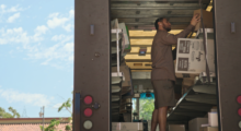 A Black male UPS worker unloads packages from the back of his truck.