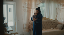 A woman in a black hijab and blue dress cradles a baby in her arms.
